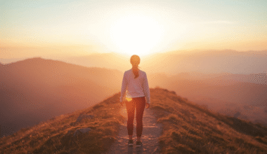 Alt Text: Person standing on mountain path at sunrise symbolizing self-improvement journey